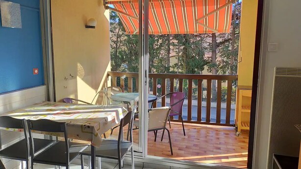 Ein Balkon mit Tisch und Stühlen, einem gestreiften Sonnensegel und Blick auf Bäume und Gebäude.