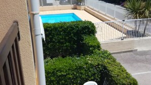 Ein Balkon mit Pool, weißen Plastikstühlen und einer Hecke.