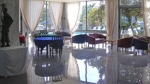 A spacious indoor area with a pool table, multiple seating areas, and large windows offering views of the outdoors. - Virginia Apartments (Rhodes)