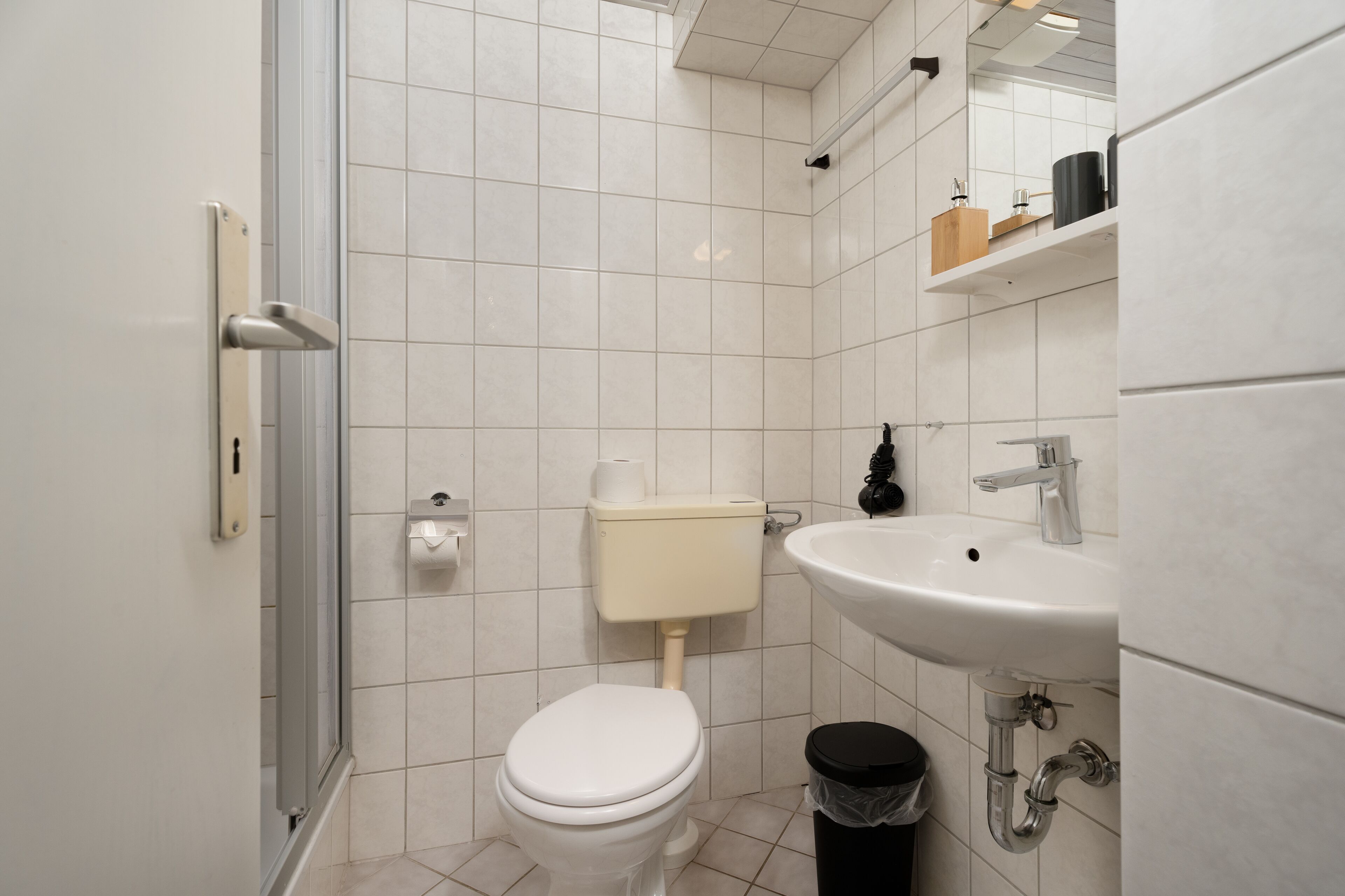 A modern bathroom with a toilet, sink, and trash bin.