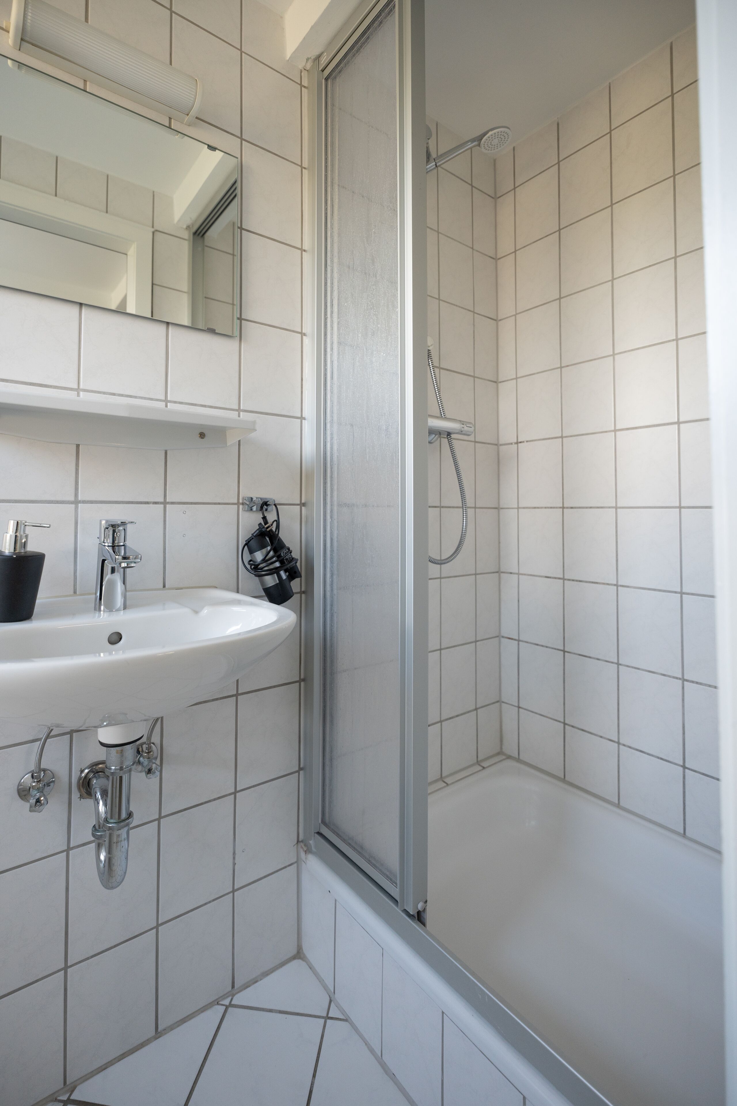A bathroom with a white sink, mirror, and shower.