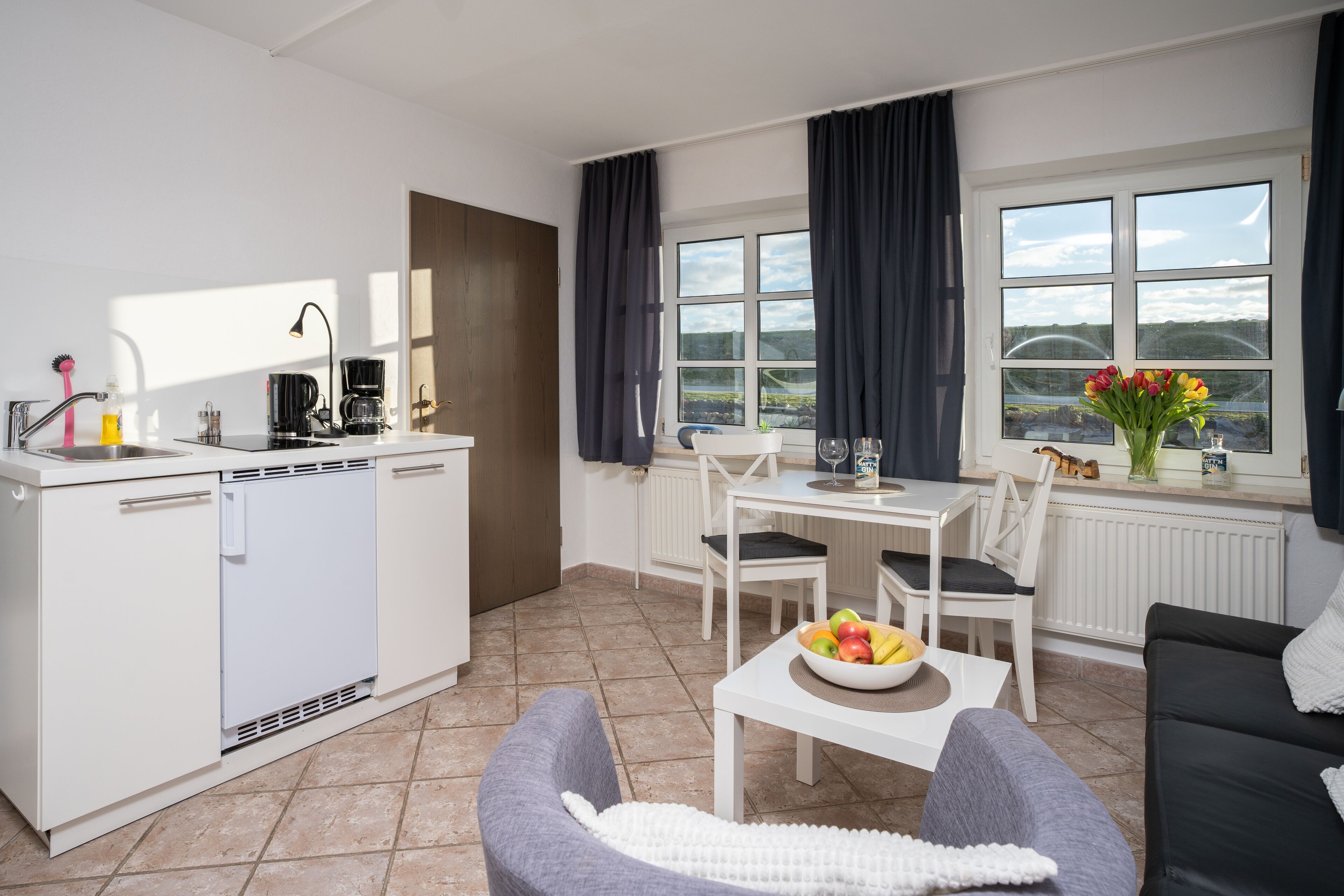 A modern kitchen with white appliances, a dining area with a table and chairs, and a sofa.