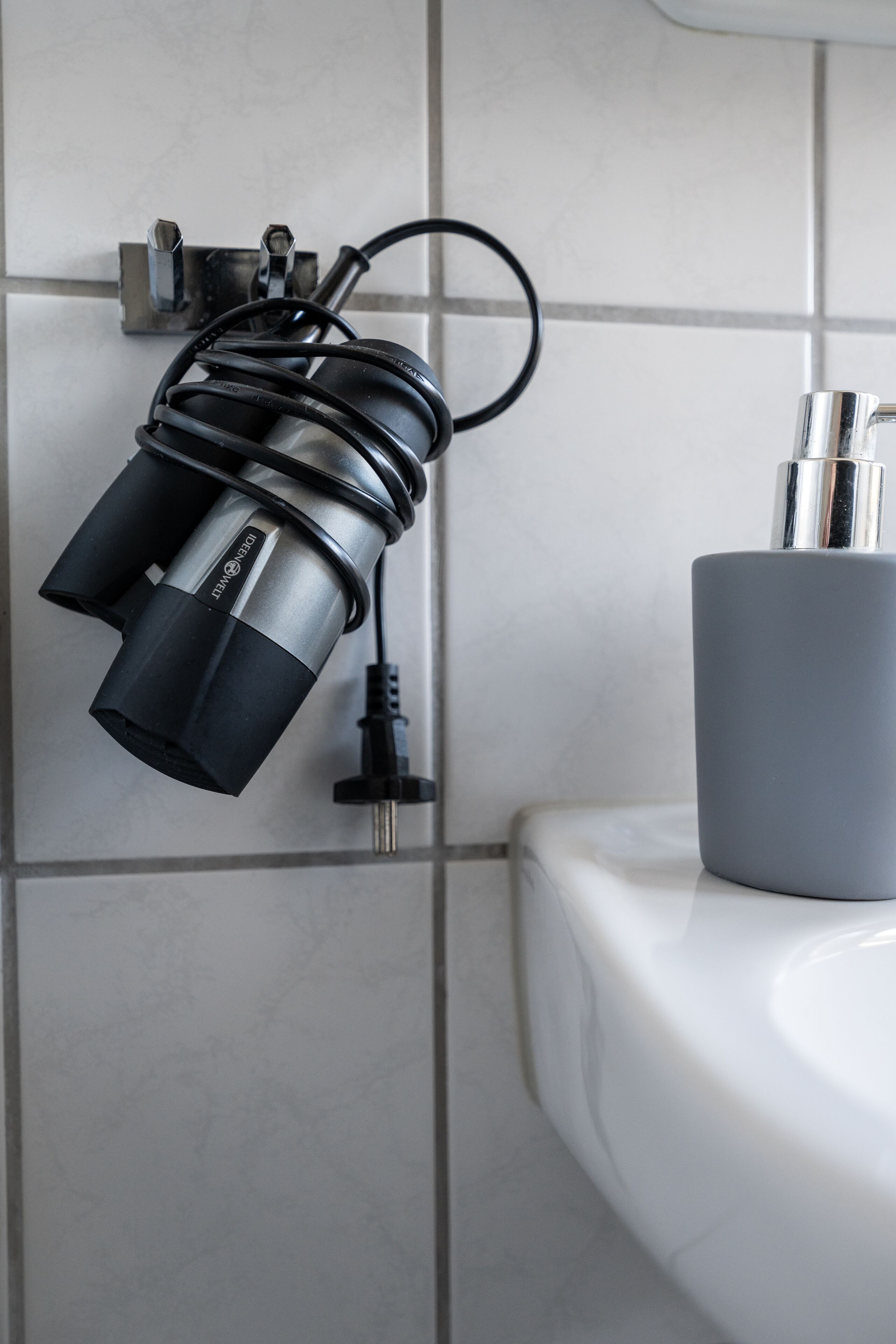 A bathroom with a wall-mounted light fixture and a gray cup holder on the sink.