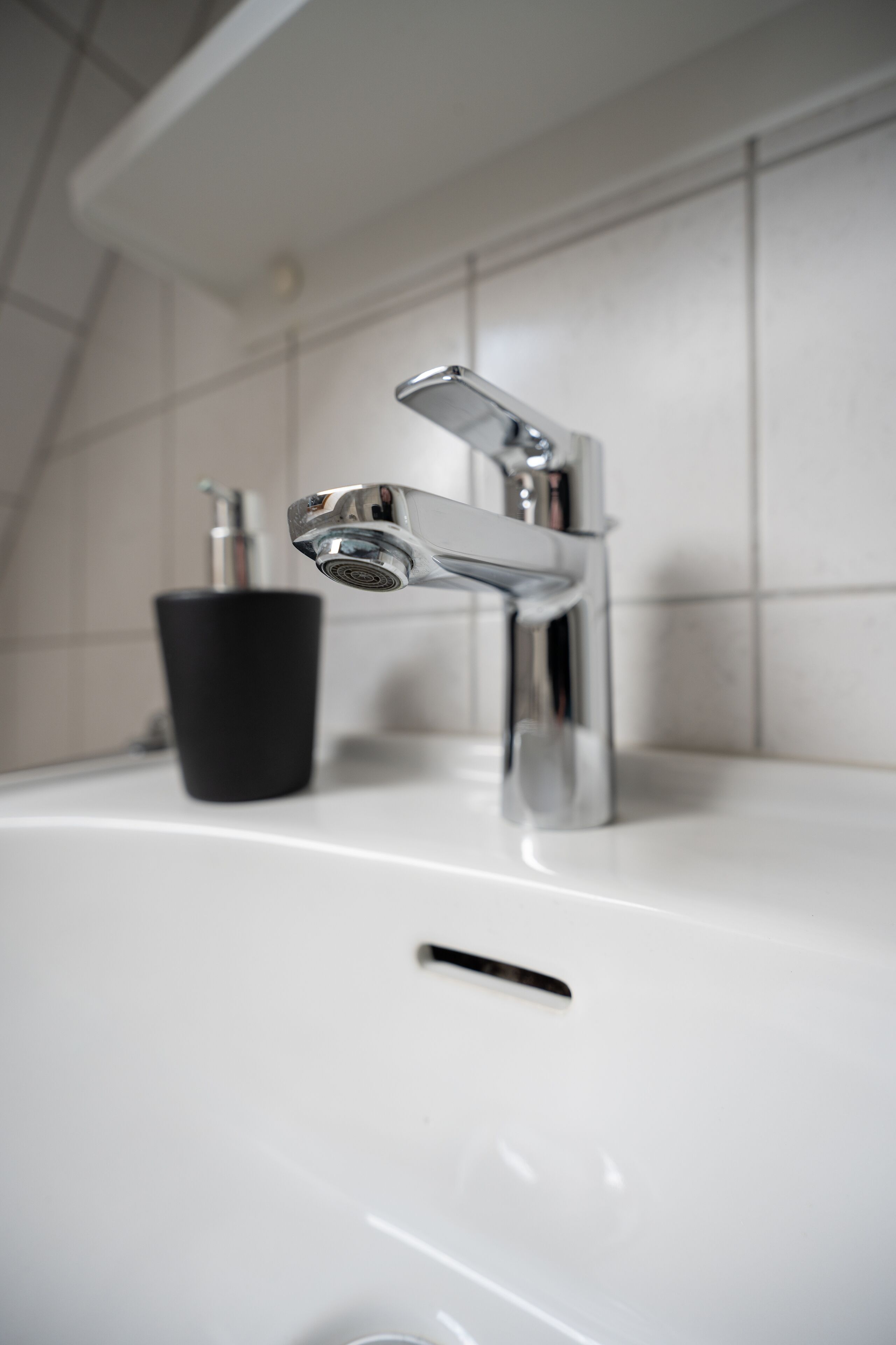 Un lavabo de salle de bain moderne, doté d’un robinet chromé et d’un distributeur de savon noir.