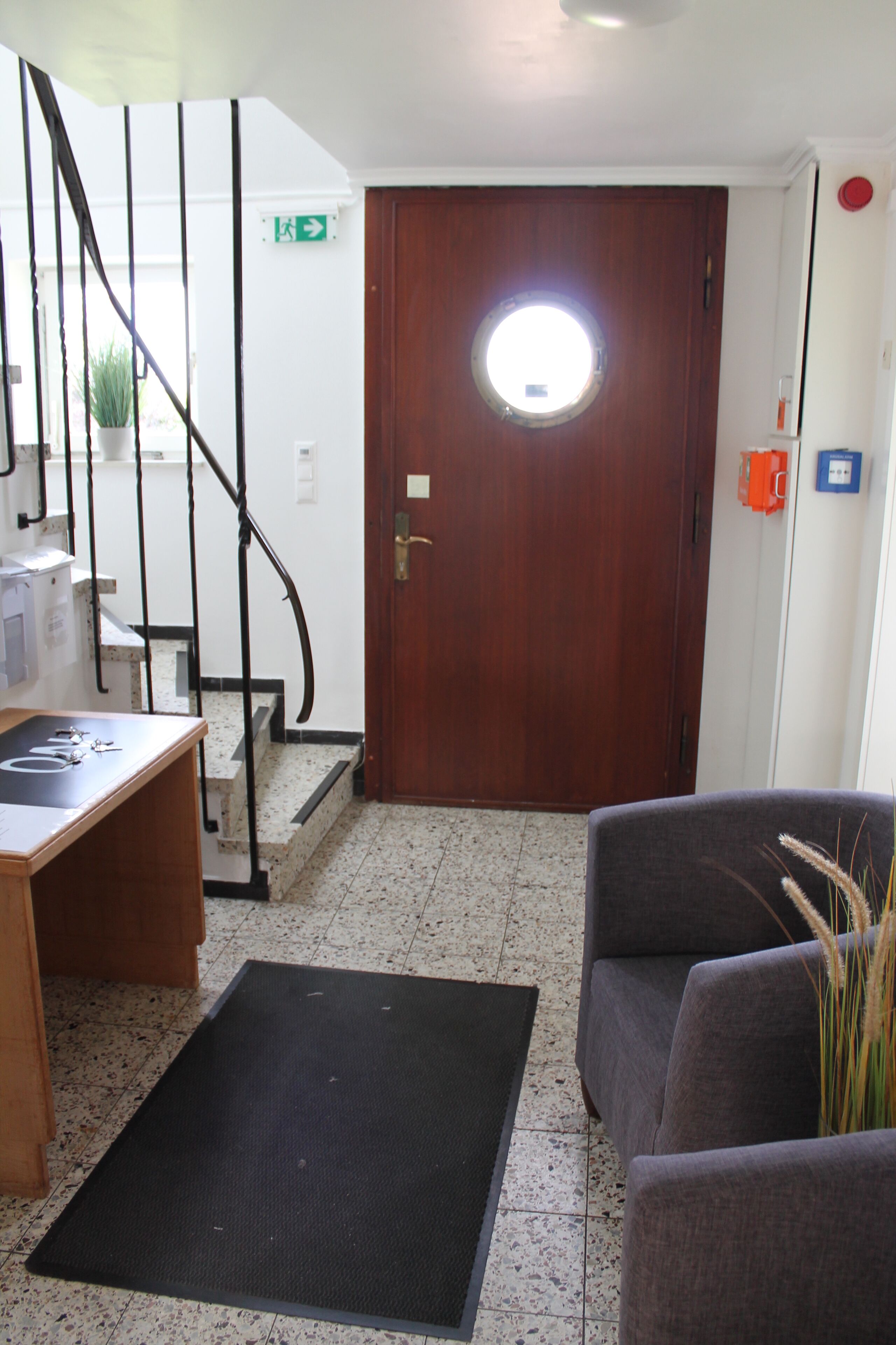 Un vestíbulo de hotel con puerta de madera, una escalera, un mostrador de recepción y una zona de estar.