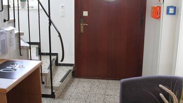 Un vestíbulo de hotel con puerta de madera, una escalera, un mostrador de recepción y una zona de estar.