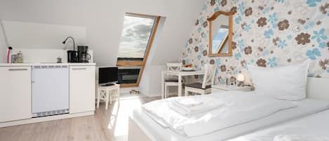 A modern bedroom with a large bed, a desk, and a kitchenette.