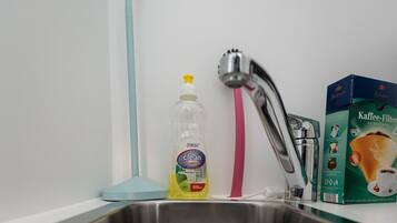 Un lavamanos de acero inoxidable con desagüe, una botella de detergente, un cepillo de limpieza rosa y una caja de filtros de café.