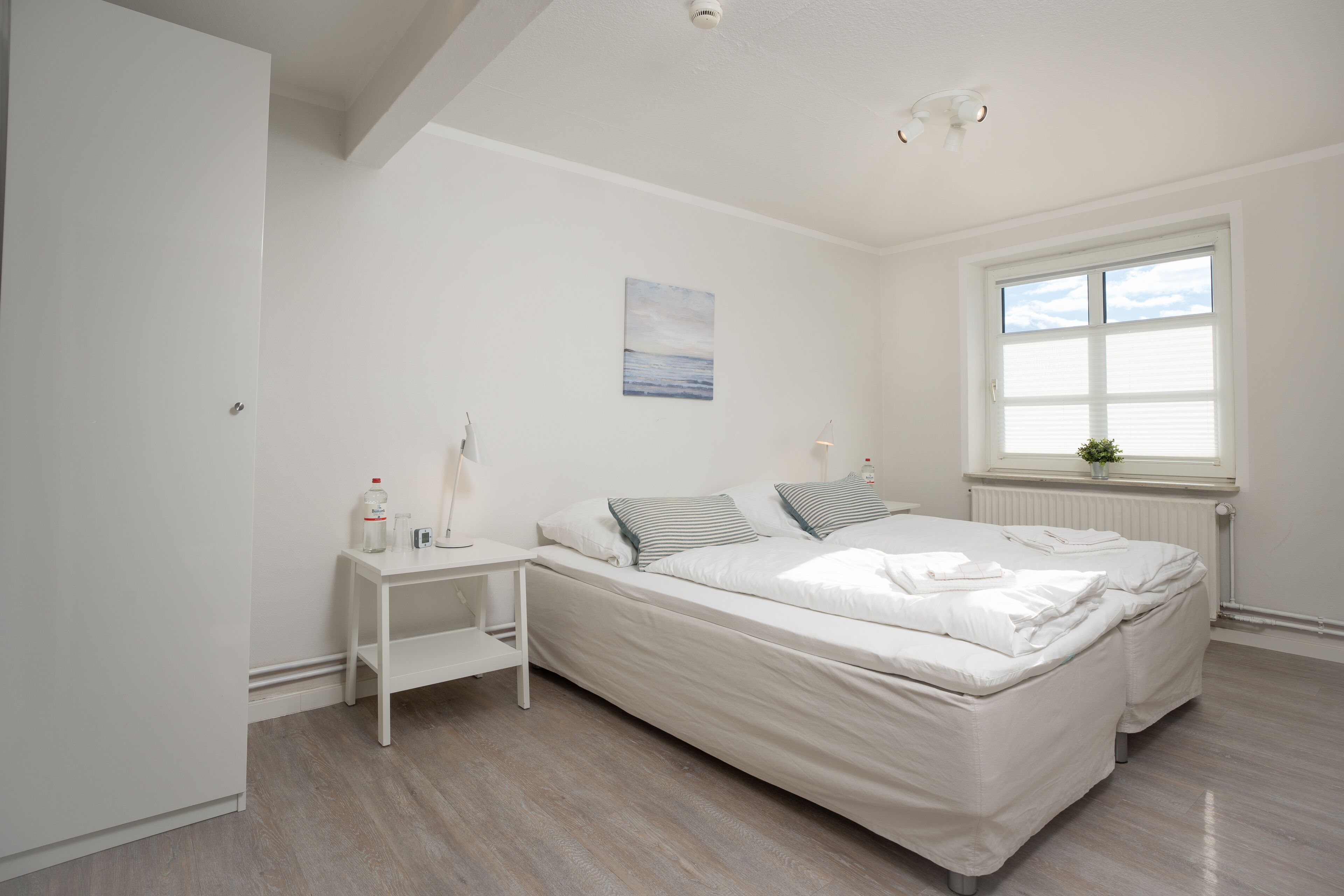 A bedroom with a bed, bedside tables, a window, and a painting on the wall.