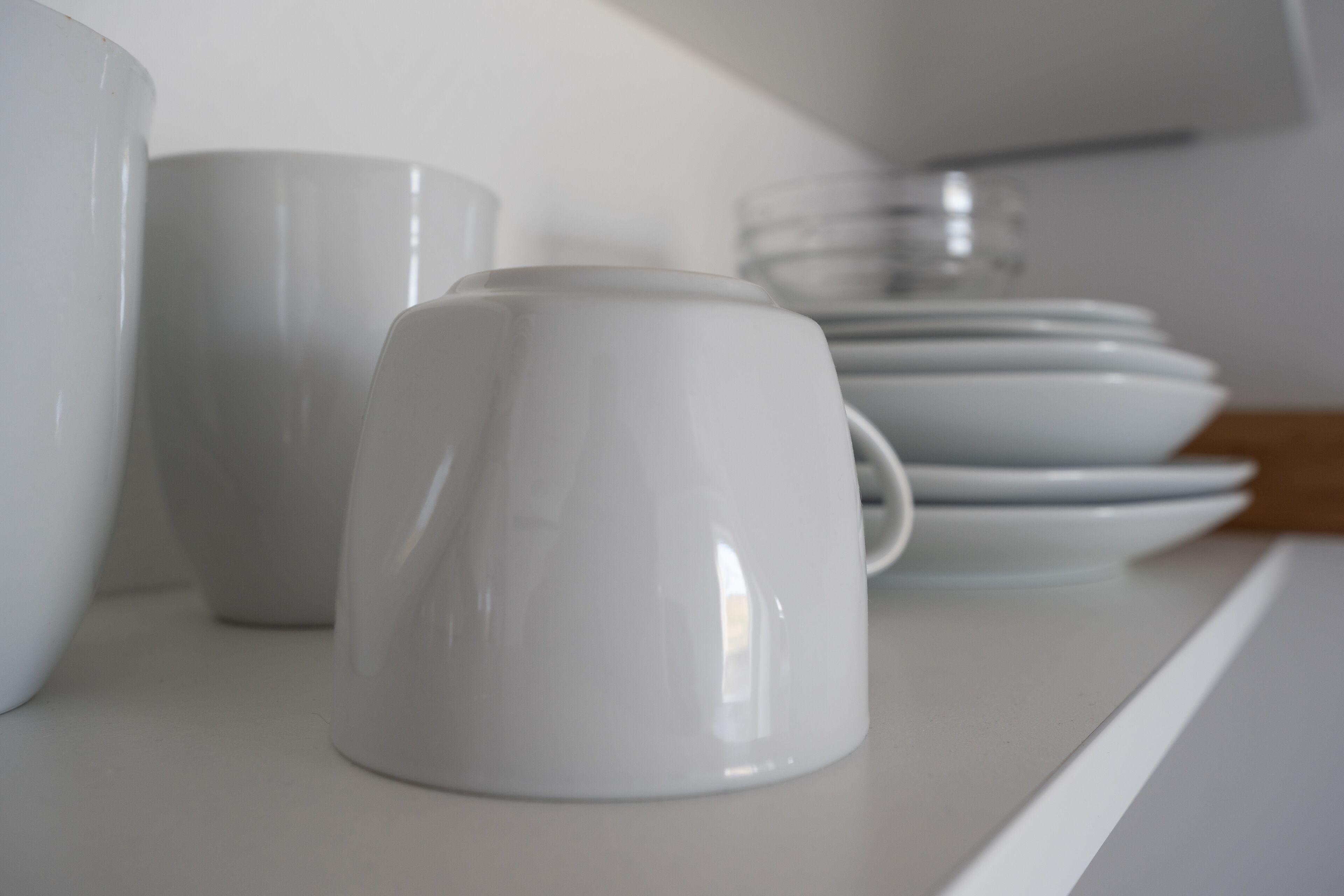 Une étagère blanche sur laquelle sont disposés divers objets en céramique blanche, notamment des tasses et des assiettes.