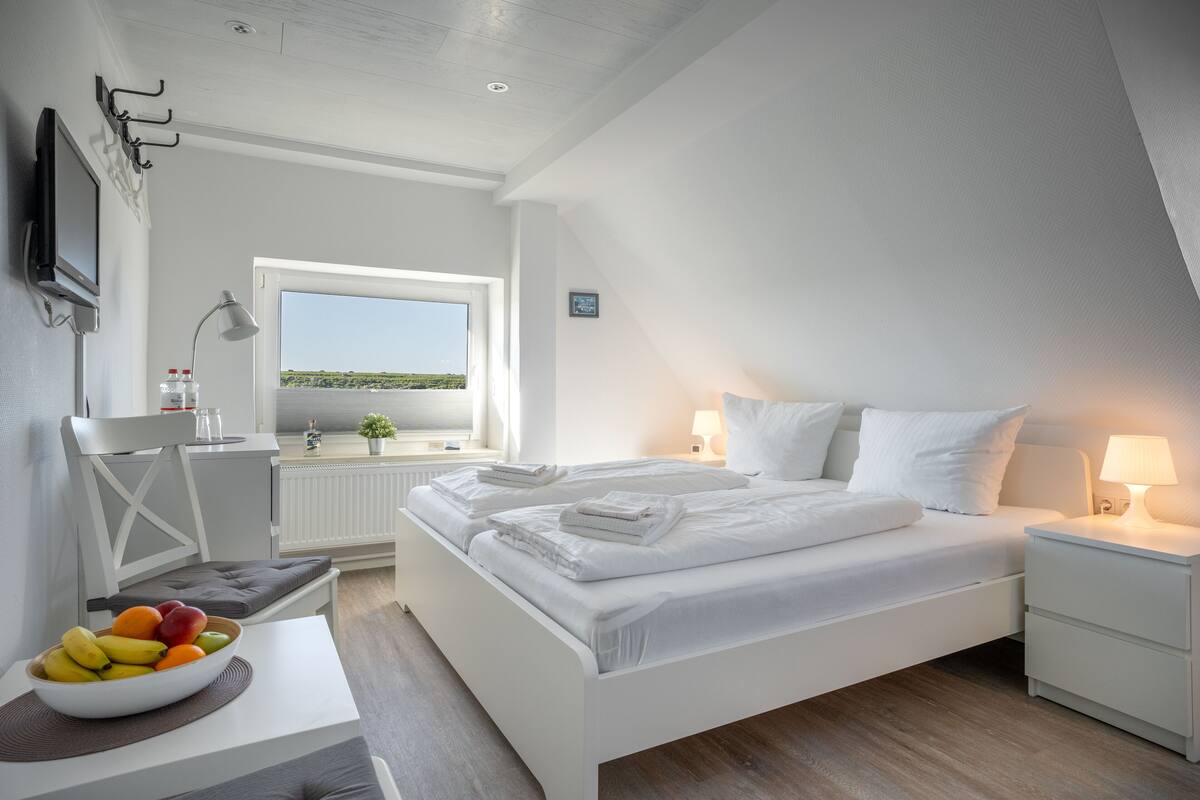 Een moderne slaapkamer met een groot bed, nachtkastjes, een bureau met een schaal fruit, een stoel en een raam met uitzicht.