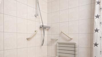 Un espacio de ducha pequeño con azulejos, un cabezal de ducha manual, un taburete pequeño y un perchero para toallas.