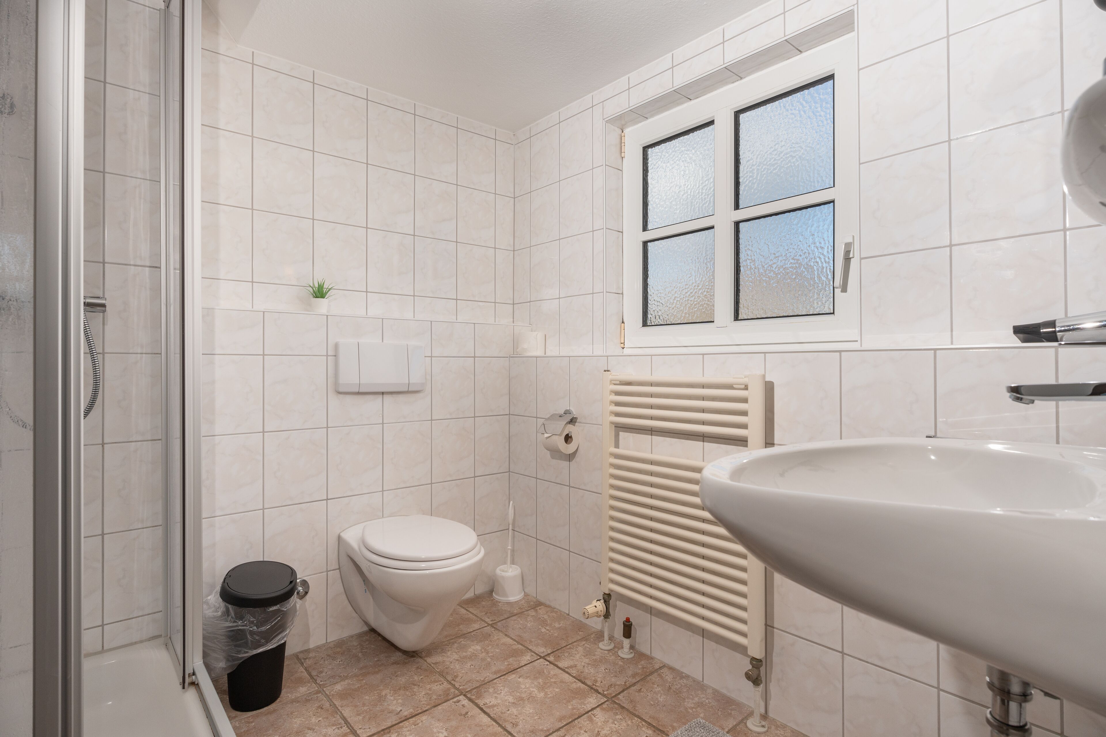 Un baño con ducha, inodoro, lavabo y ventana con vidrio esmerilado.