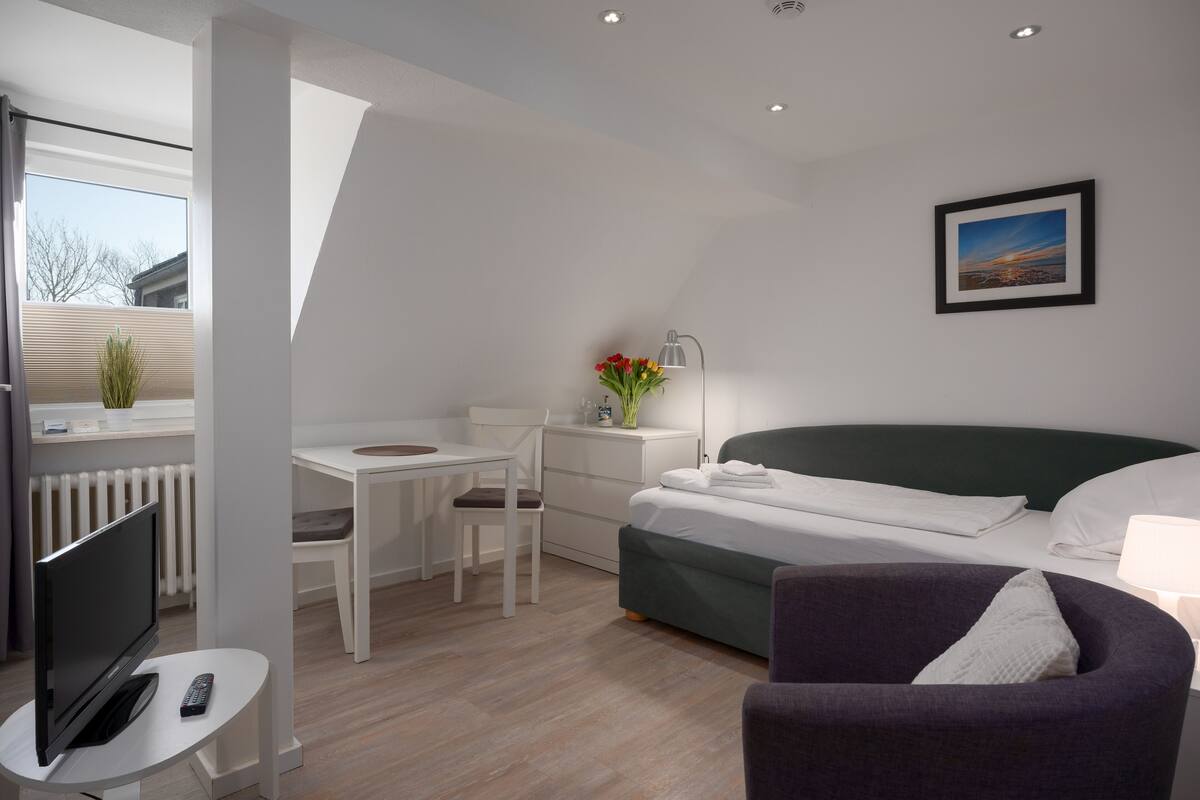 Een moderne kamer met een bed, een bureau, een stoel, een televisie en een raam.