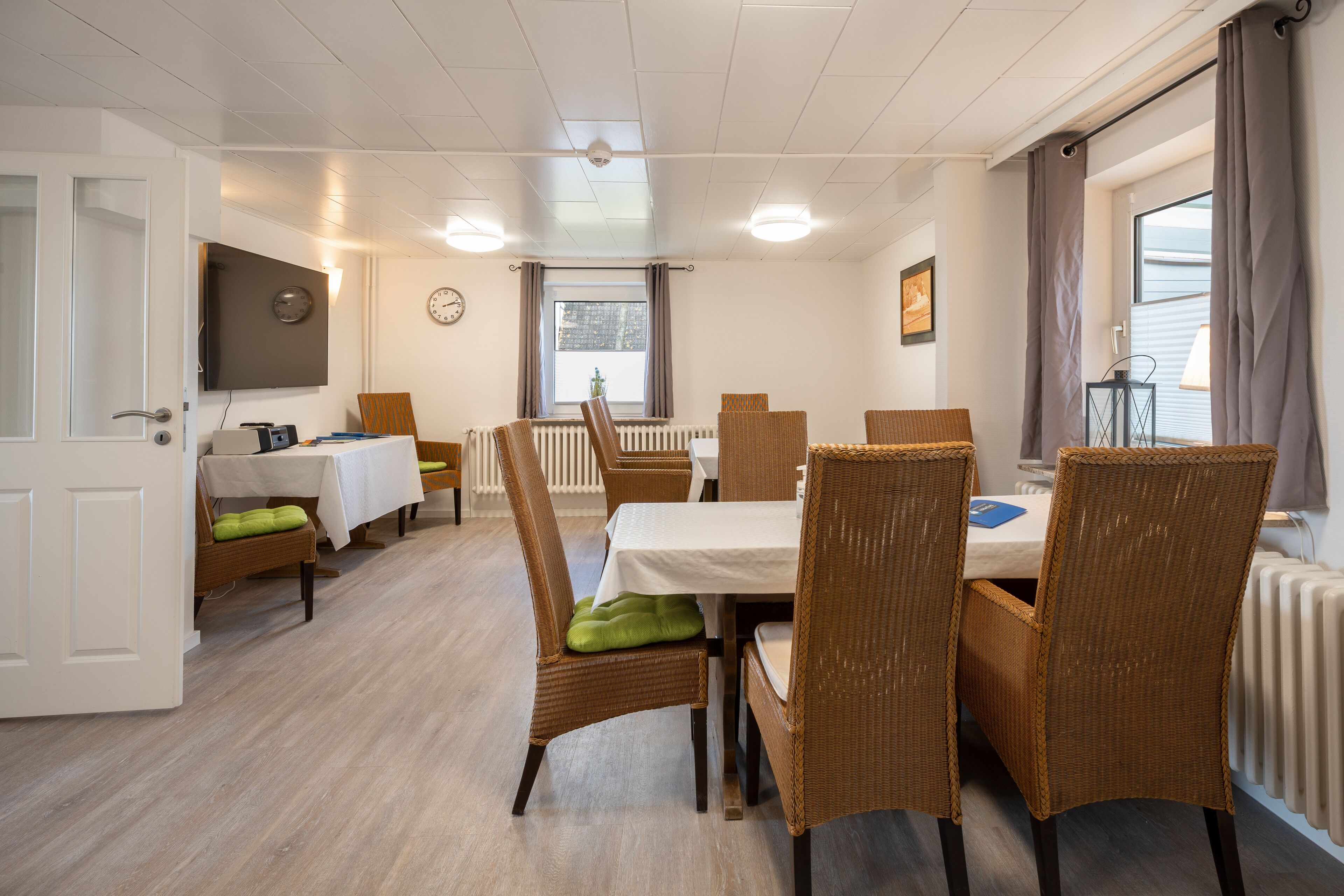 A dining area with wicker chairs, a white table, and a clock on the wall.