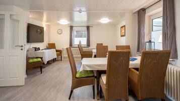 A dining area with wicker chairs, a white table, and a clock on the wall.