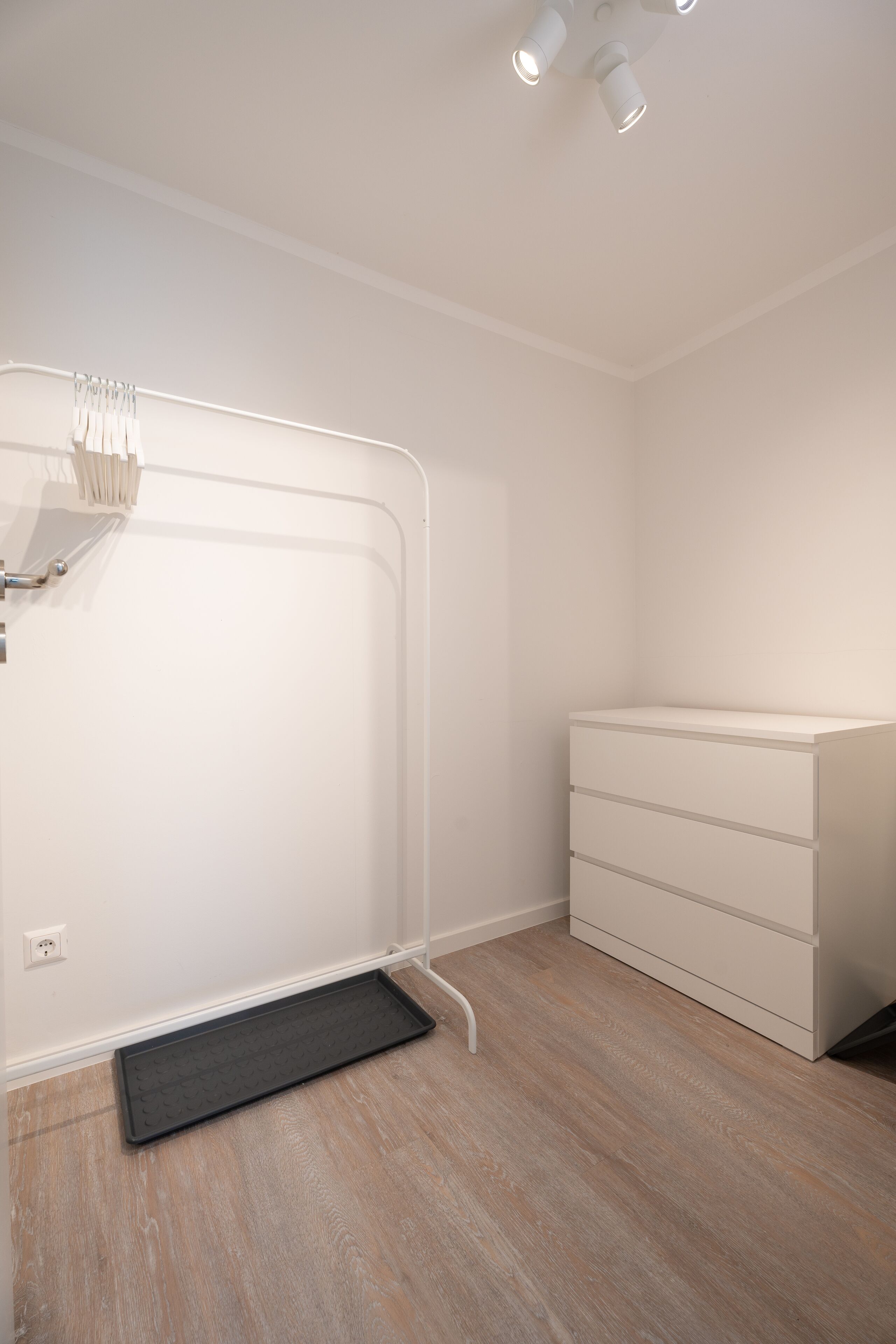 A room with a white wardrobe, a black mat at the entrance, and a ceiling light fixture.