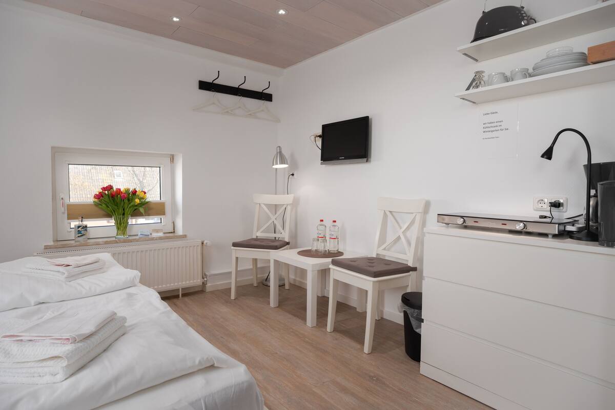 Een moderne hotelkamer met een bed, twee stoelen, een klein tafeltje, een televisie en een kitchenette.