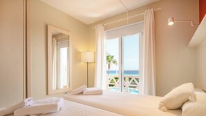 A hotel room with two beds, a large window with a view of the sea, and a balcony. - Apartment 4 In front of the sea (Urbanització Santo Tomás, Es Migjorn Gran)