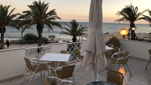 A terrace with tables and chairs overlooking the sea, palm trees, and a sunset. - Borda D Agua Apartments (Albufeira)