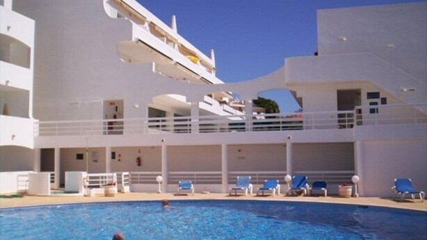 A swimming pool with lounge chairs and a building with multiple balconies. - Borda D Agua Apartments (Albufeira)