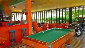 A pool table in a room with checkered flooring, a bar area, and a vintage car. - La Fenice (Jesolo)