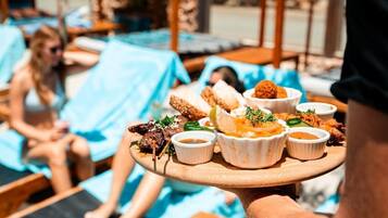 Una bandeja de comida servida en un área junto a la piscina, con sillones de descanso y la piscina al fondo.