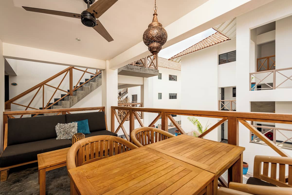 A spacious balcony with a wooden table and chairs, a sofa with cushions, and a decorative hanging light fixture.