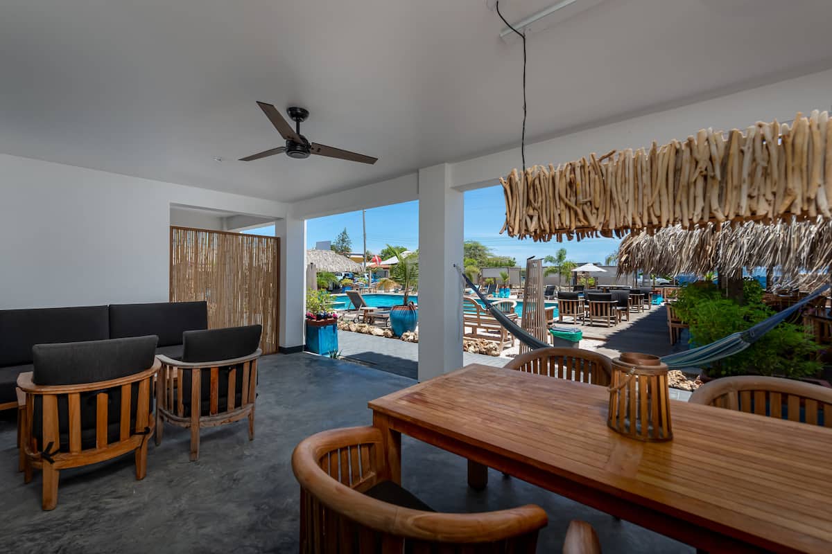A modern indoor space with a wooden dining table and chairs, a ceiling fan, and a view of an outdoor pool area.