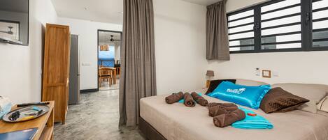 A hotel room with a bed, a desk, a ceiling fan, and a view of the sea through the window.