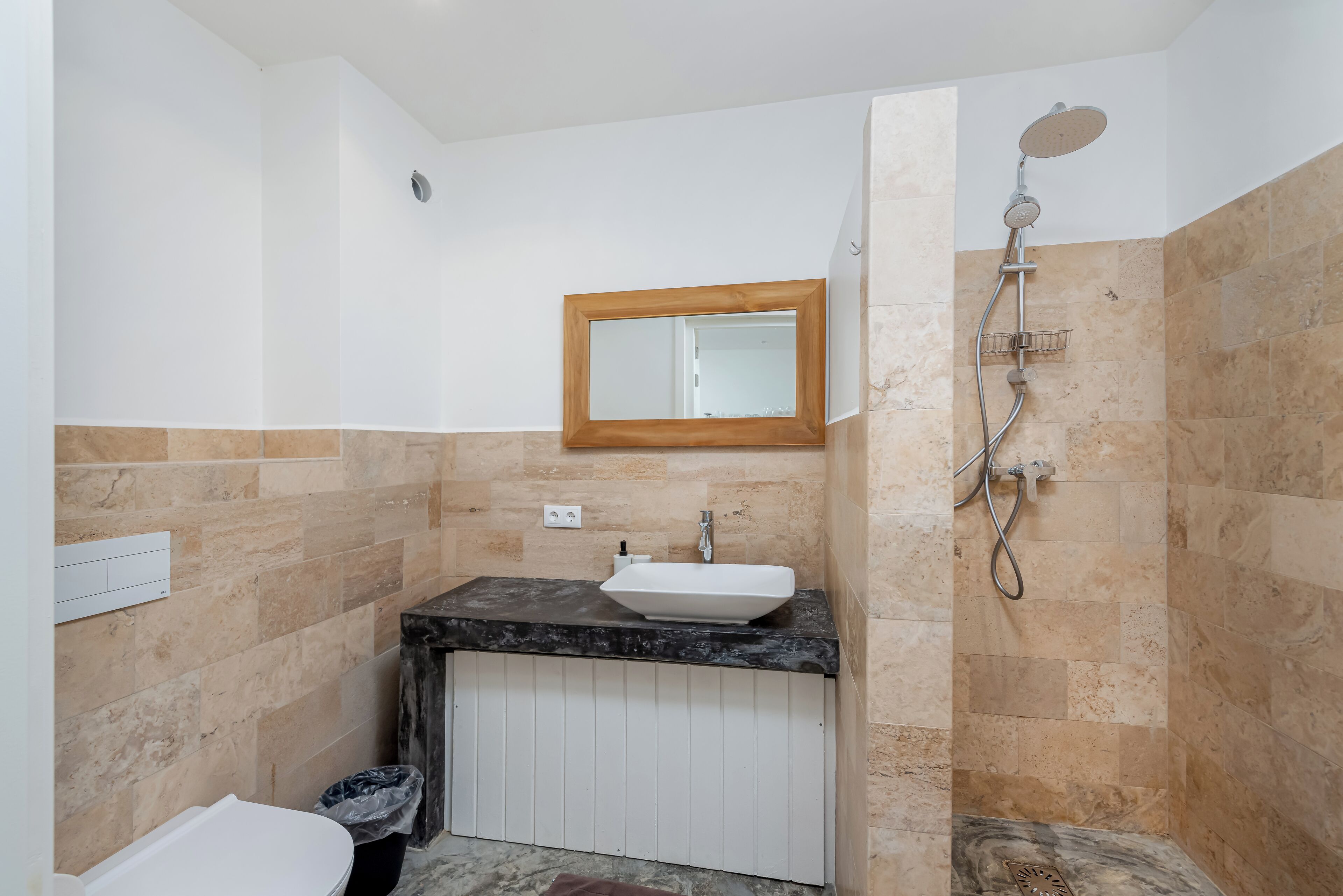 Un baño con lavamanos blanco, un espejo con marco de madera y zona de ducha.