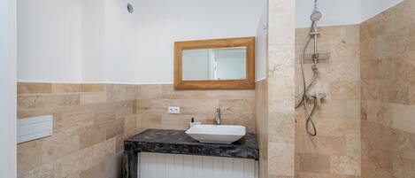 Un baño con lavamanos blanco, un espejo con marco de madera y zona de ducha.