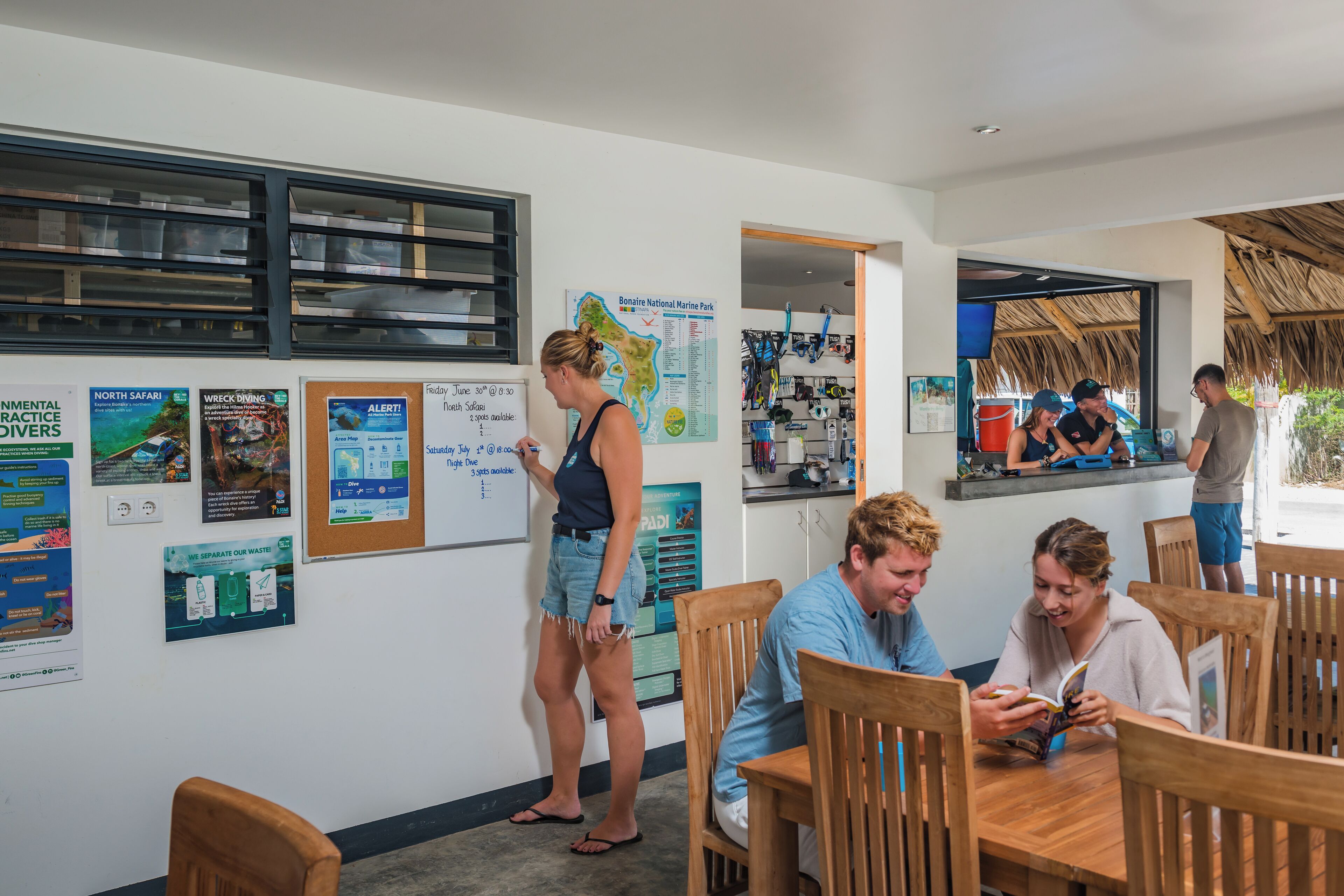 Un restaurant avec des tables et des chaises en bois, un tableau affichant le menu et diverses affiches au mur.