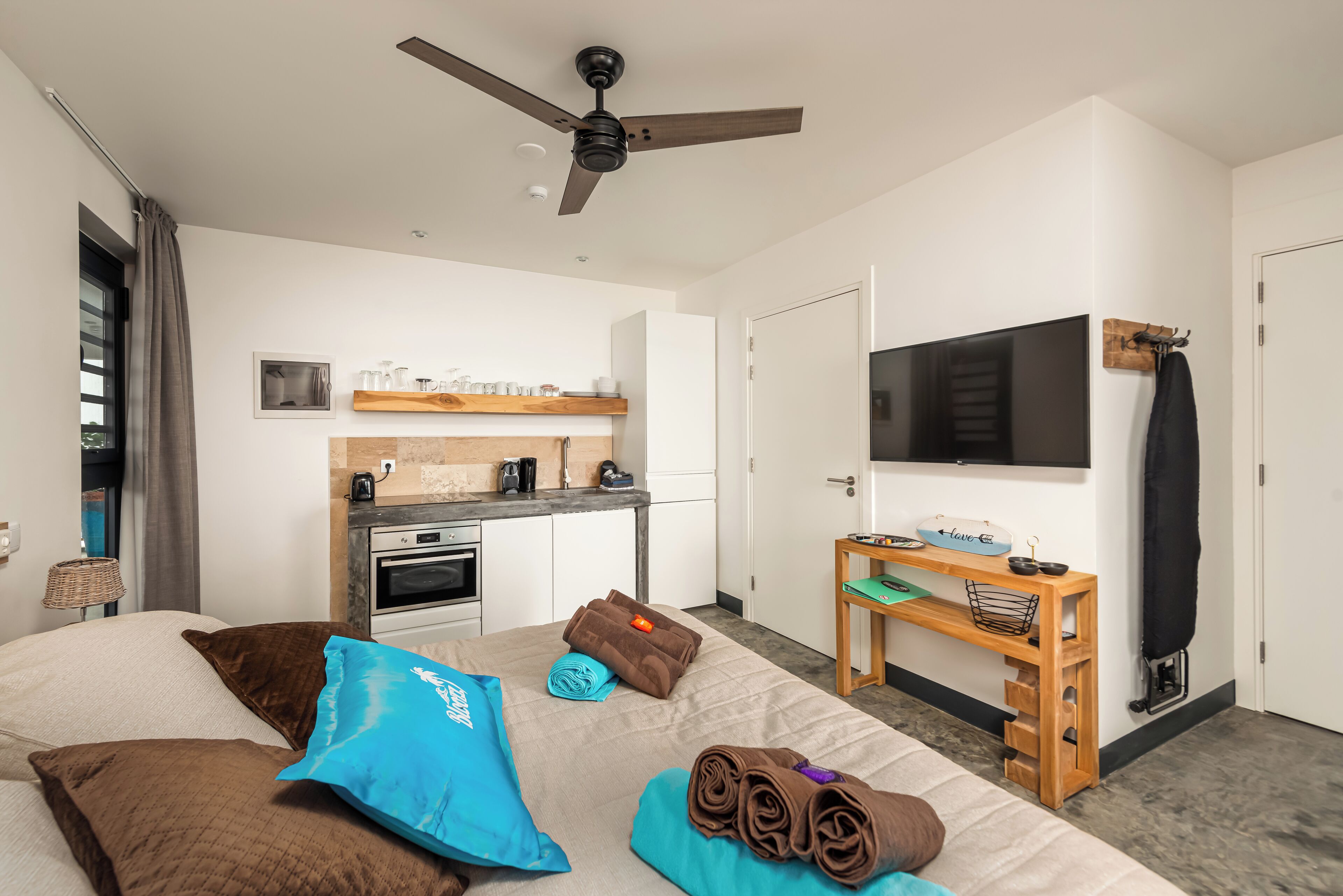 A modern hotel room with a bed, a desk, a TV, and a kitchenette.