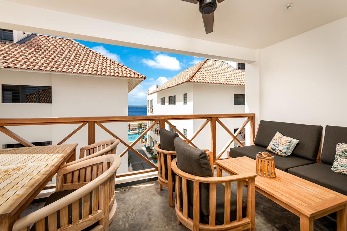 A balcony with wooden furniture, a sofa, and a view of the sea and buildings.