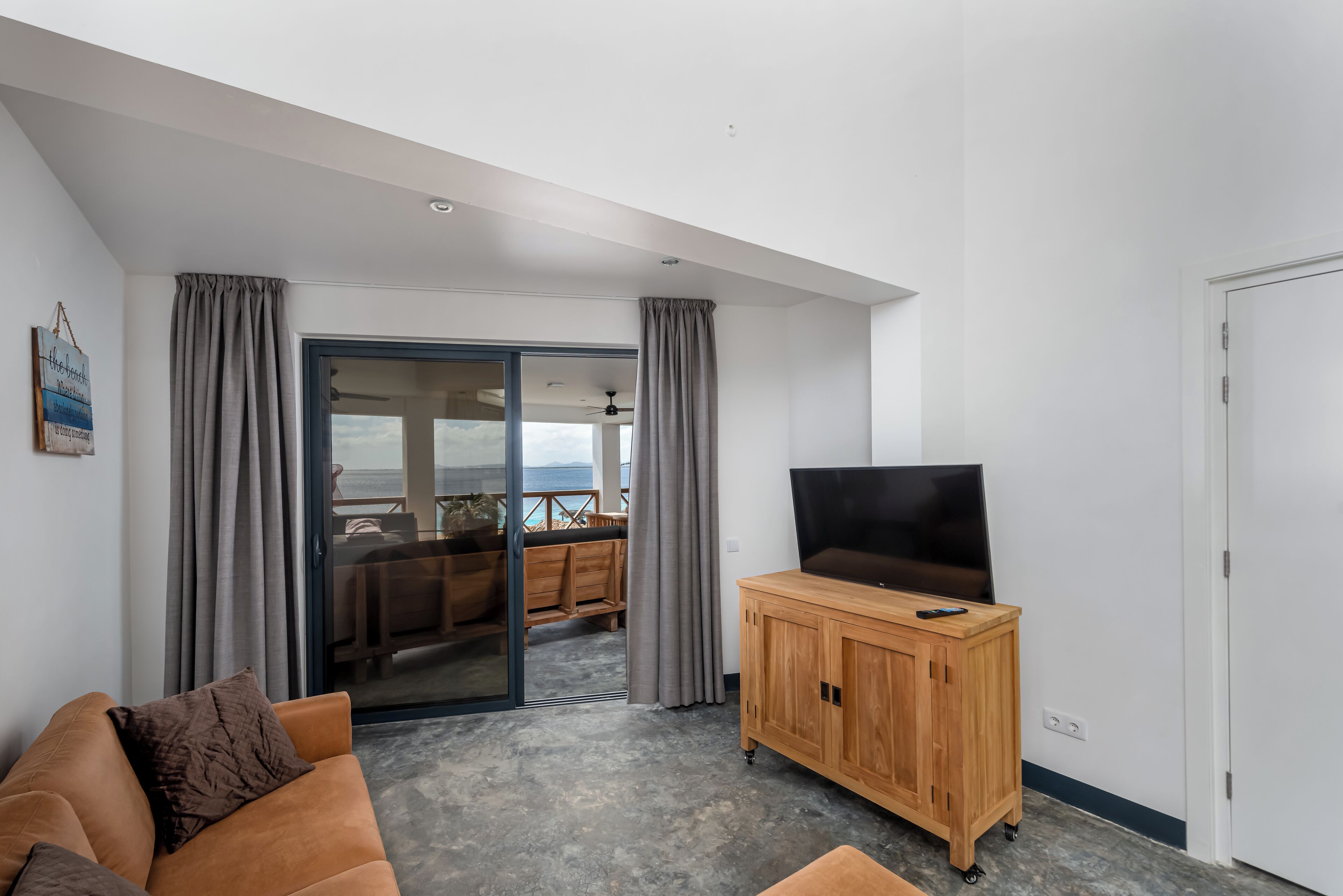 A modern living room with a sofa, a wooden TV stand, and a sliding glass door leading to a balcony.
