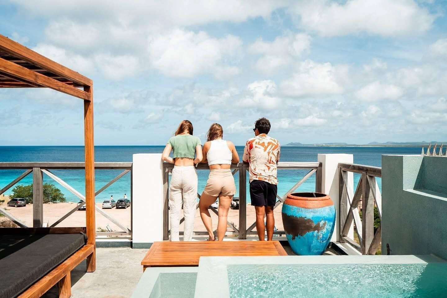A balcony with a view of the ocean, a wooden bench, and a large vase.