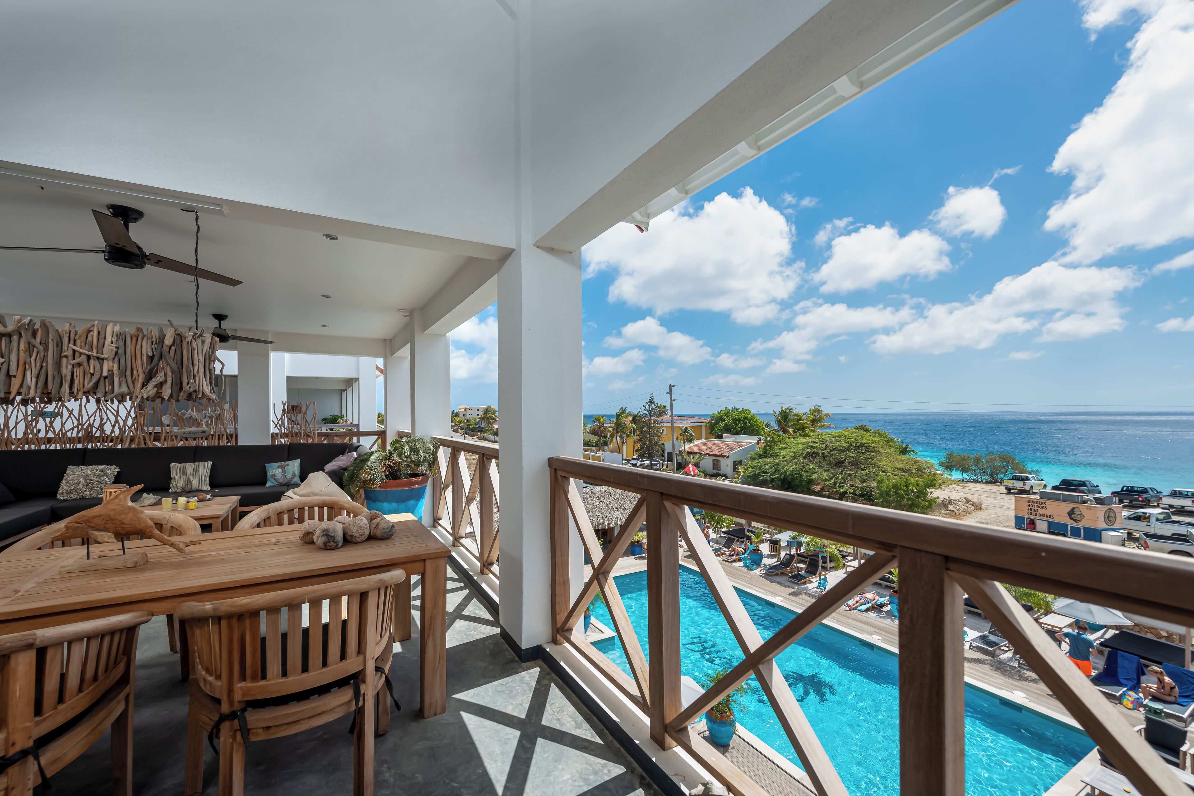 Terraza de madera con vista a la piscina, con zona de comedor, sillas y una mesa, y un ventilador de techo.
