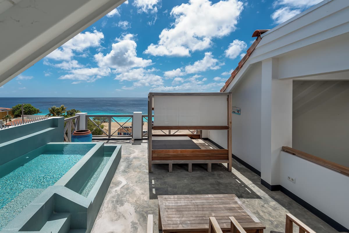 A rooftop pool area with a view of the ocean, a wooden deck, and a covered seating area.