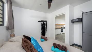 Une chambre à coucher avec un lit, des oreillers, un ventilateur de plafond, un porte-serviettes et une vue sur la cuisine.
