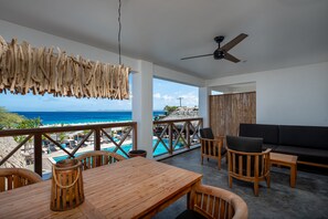 A wooden table and chairs on a balcony overlooking a pool and the ocean. - Bloozz resort Bonaire (Kralendijk)