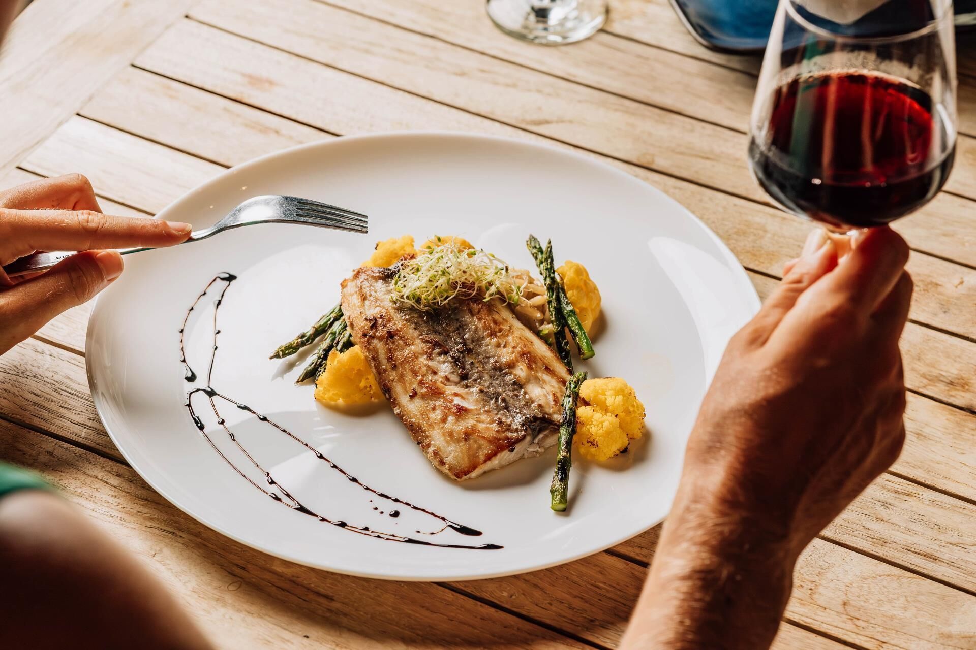 Ein Teller mit Essen, eine Gabel und ein Glas Rotwein auf einer Holztisch.