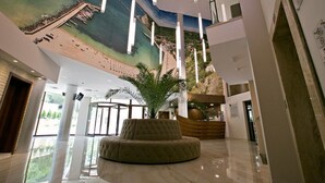 Un vestíbulo amplio con una zona de estar grande, una recepción y un mural con una escena de playa en el techo.