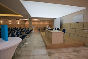 A conference room with a long table, chairs, a podium, and a whiteboard. - Royal Grand Hotel & Spa (Kavarna)