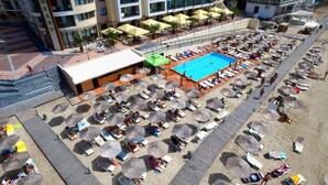 Zona de piscina en la azotea con tumbonas y sombrillas, rodeada por un edificio con balcones.