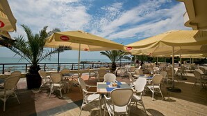 Un café al aire libre con mesas, sillas, sombrillas y vistas al mar.