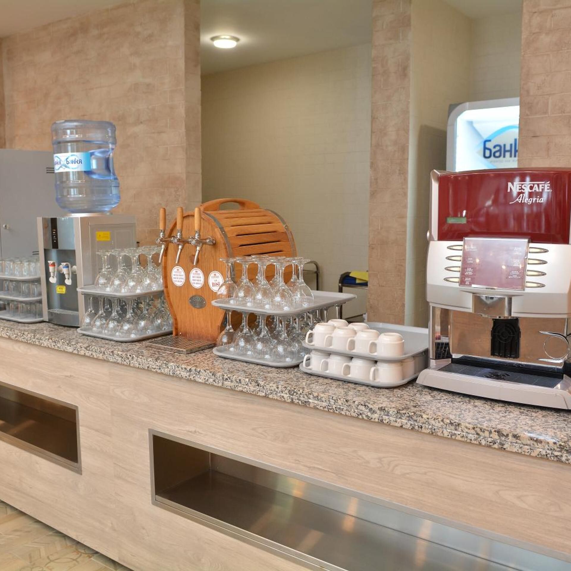 Un mostrador de desayuno de hotel con dispensadores de agua, una máquina de café y vasos.