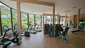 A gym with exercise equipment, large windows, and a view of greenery. - Royal Grand Hotel & Spa (Kavarna)