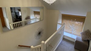 A staircase with a white railing, a chandelier, a mirror, and a window with blinds.