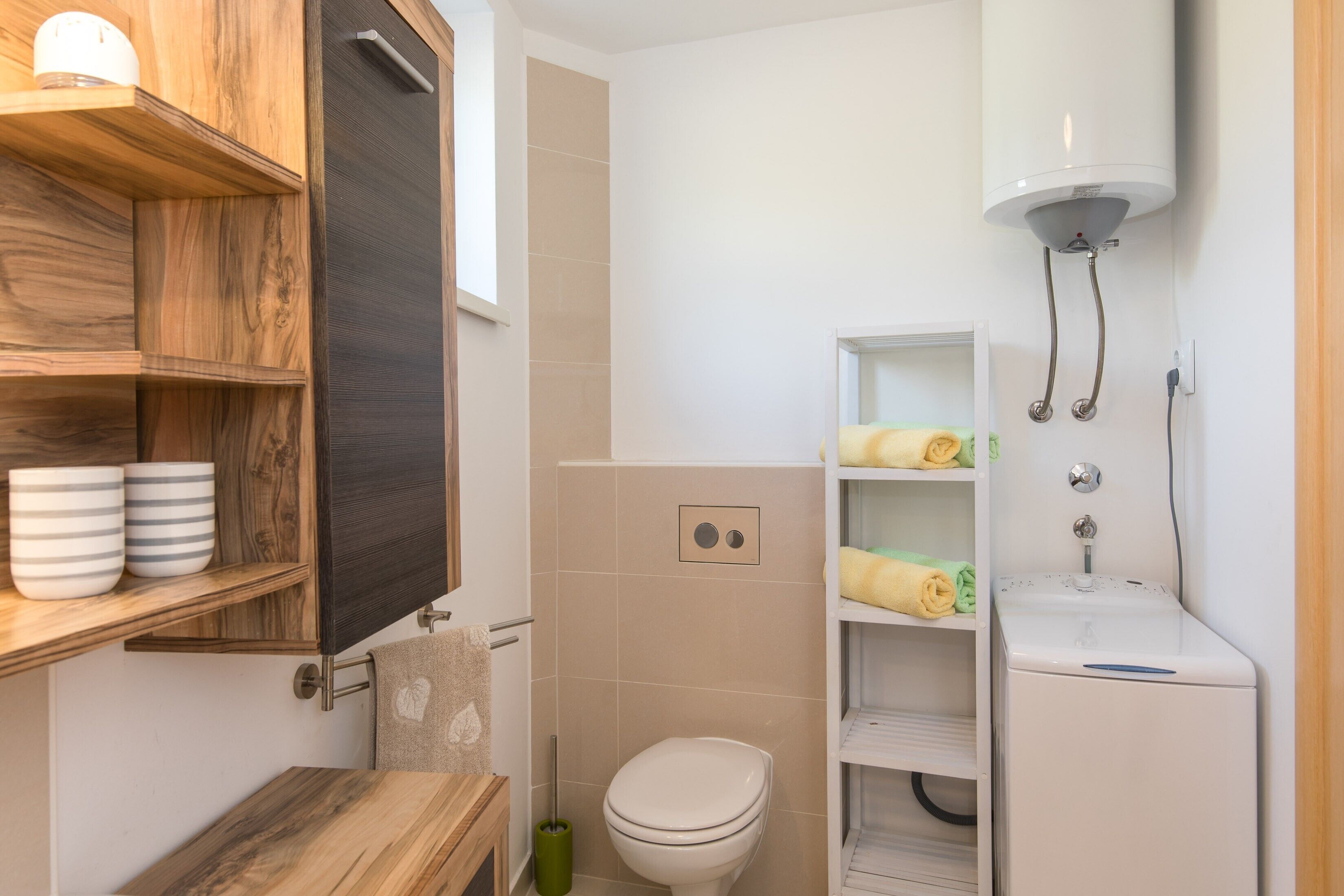 Une salle de bain comprenant des toilettes, un lavabo, une douche, des étagères en bois avec des bols et un porte-serviettes.